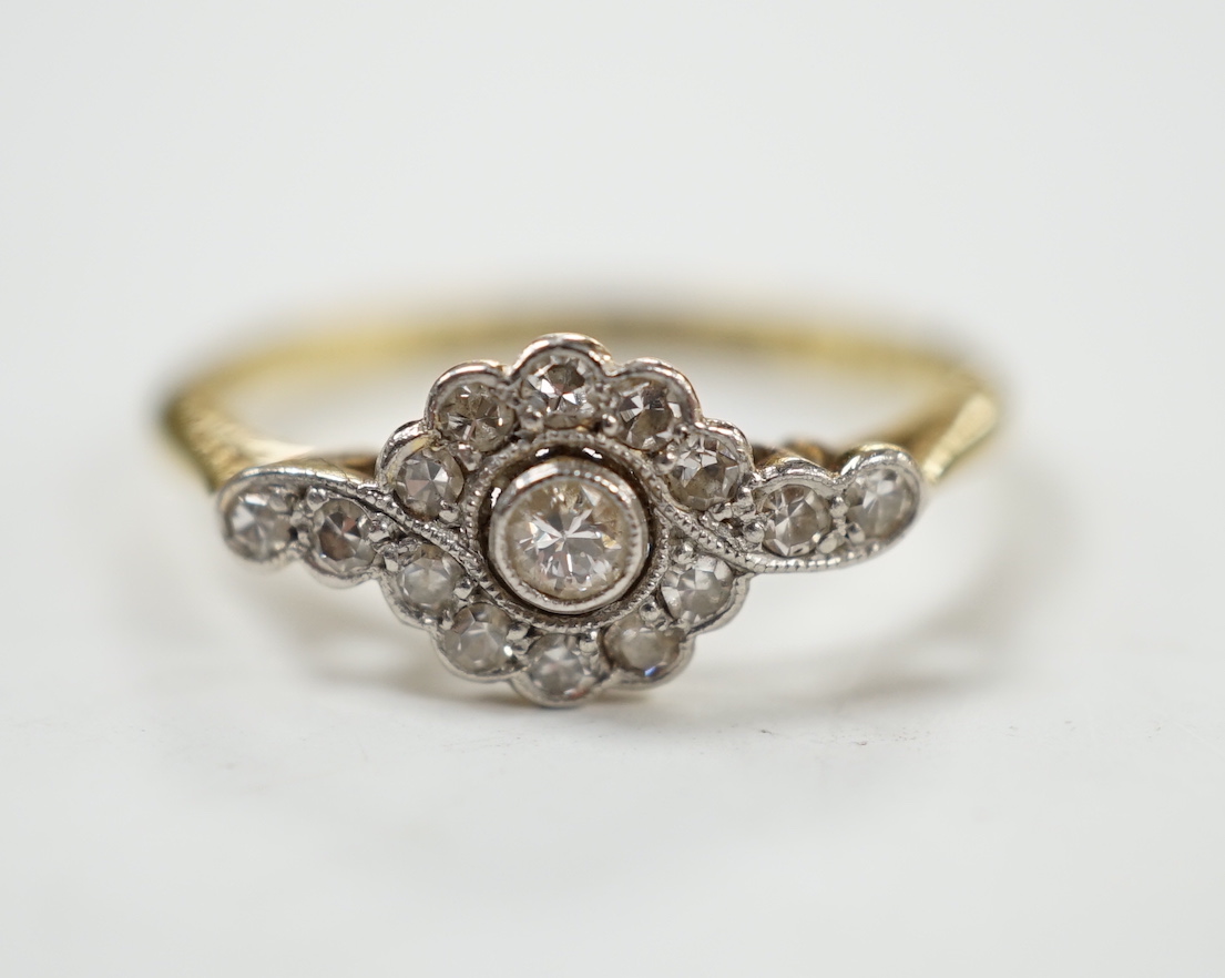 A Belle Epoque 18ct, plat and diamond cluster set target ring, with diamond set shoulders, size P, gross weight 2.6 grams.